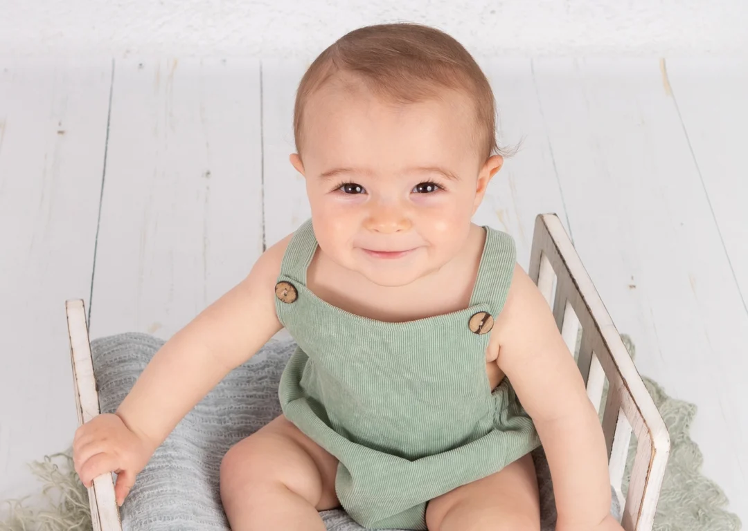 Fotografía de bebé de 8 meses sentado en una camita sonriendo durante su sesión de fotos en estudio en Madrid.
