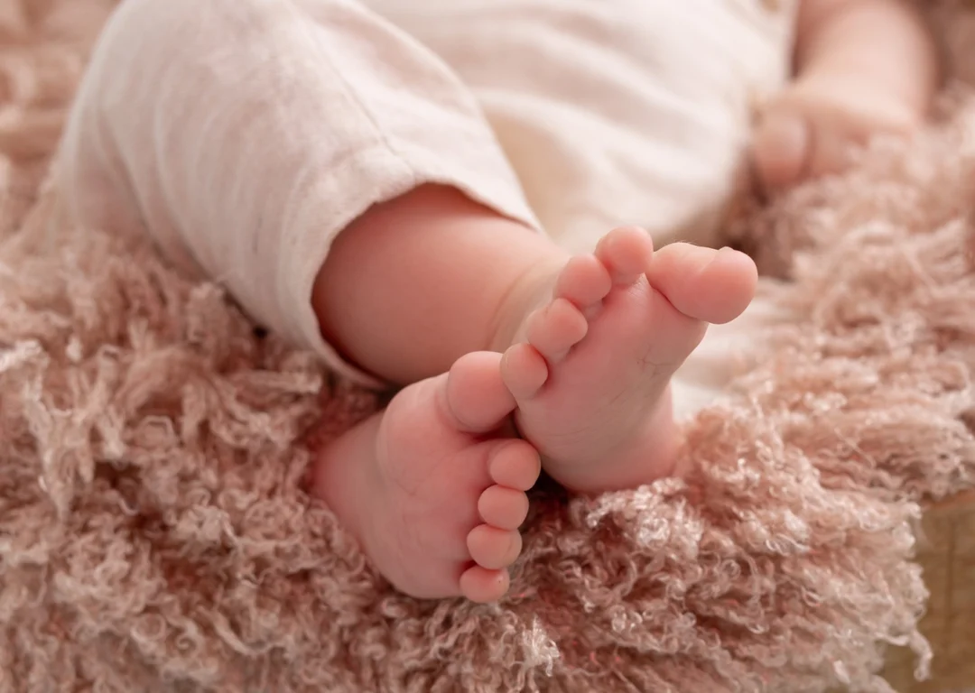 Fotografía macro de los pies descalzos de un bebé sobre una manta suave en sesión de fotos infantil.