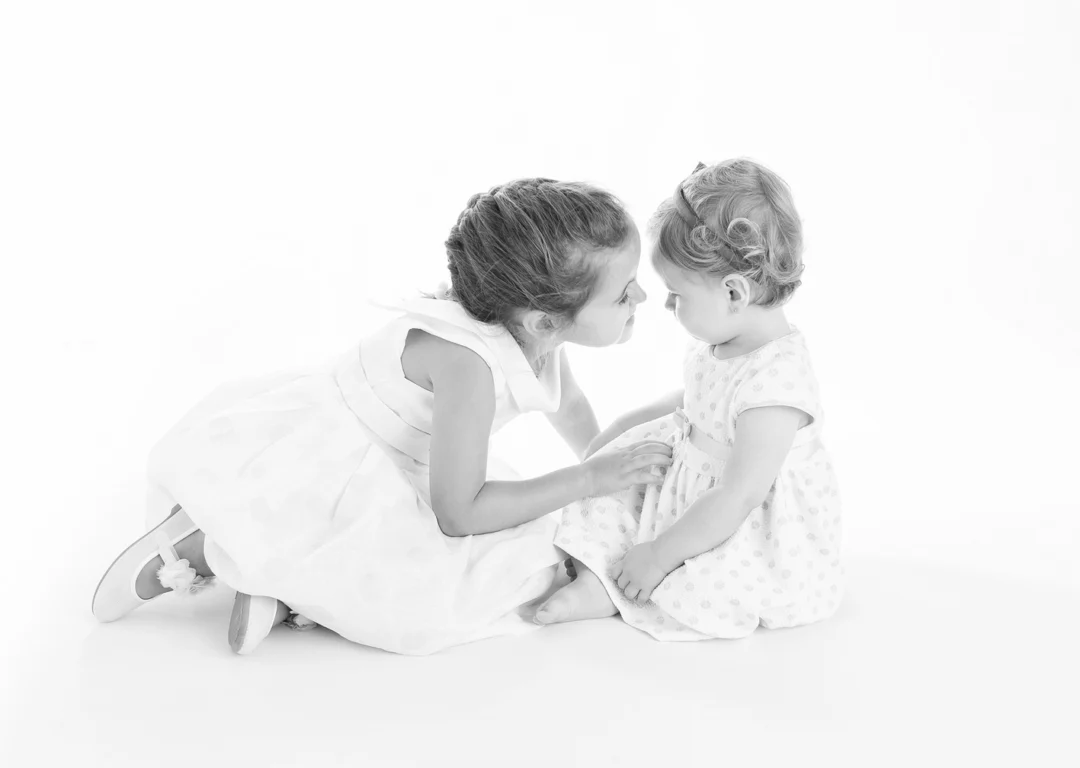 Hermana mayor dando un beso a su hermanita bebé de 8 meses en un reportaje fotográfico infantil natural en Collado Villaba.