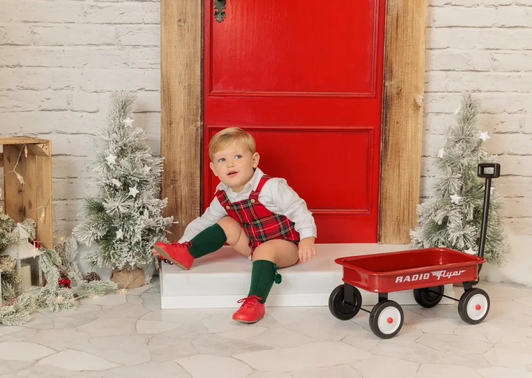 Bebé en sesión de fotos de Navidad junto a puerta roja decorada en estudio de Guadarrama